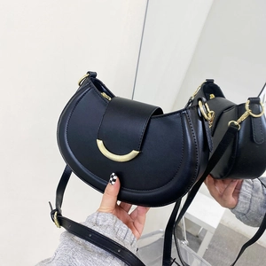 Detail of a black crescent crossbody bag featuring a golden half-moon metal buckle closure