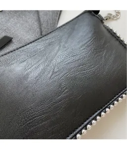 Macro detail of black pebble leather texture and silver bead trim on a handbag strap