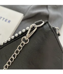 Macro detail of black pebbled leather bag with silver hooks, chain, and studded rivets
