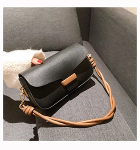Detail of minimalist black crossbody bag with brown braided handle and leather flap closure