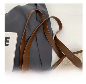 Detail of beige canvas tote bag with brown leather handle on a grey suit backdrop
