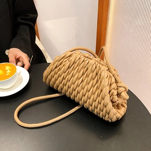 Close-up of beige woven pleated handbag with dual round handles in a cafe setting