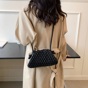 Detail of black quilted crossbody bag with drawstring strap on trench coat outfit
