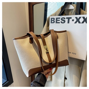 Detail of high-capacity tote bag featuring beige canvas with brown leather trim and lock