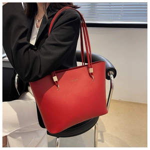 Detail of red leather tote bag showing gold stamped logo and metallic square hardware