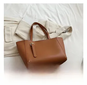 Détail du cabas en similicuir caramel avec boucle dorée sur fond de tissu blanc
