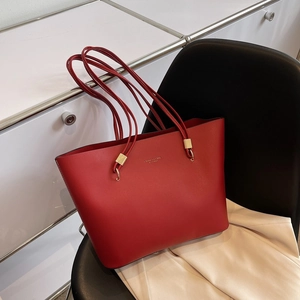 Minimalist red faux leather tote bag with gold metal hardware on a modern black chair