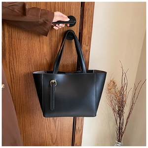 Détail du sac fourre-tout noir avec boucle en métal doré sur une porte en bois