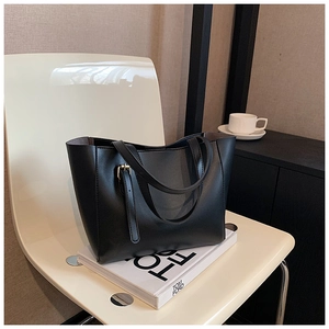 Détail de la boucle latérale du sac fourre-tout en cuir noir mat sur la chaise