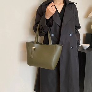 Sac fourre-tout en cuir vert olive avec boucle dorée porté avec un manteau noir