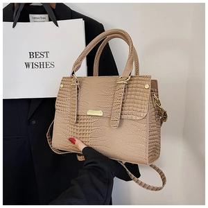 Detail of khaki crocodile pattern handbag with gold hardware held by a model