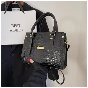 Close-up of black crocodile pattern leather handbag with gold metal clasp and strap