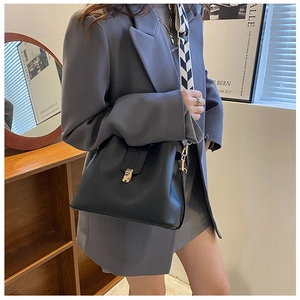 Detail of black leather shoulder bag featuring a gold buckle and geometric woven strap