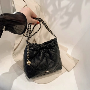 Detail of black quilted bucket bag with gold chain strap and drawstring closure