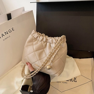 Detail of beige quilted bucket bag showing leather texture and gold chain strap