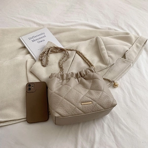 Detail of beige quilted chain bag with lychee texture and gold hardware on white fabric