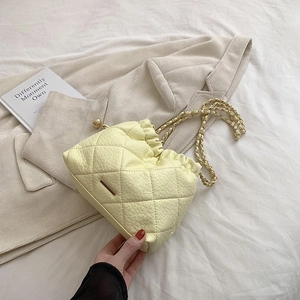Detail of yellow quilted cloud bag with gold chain strap on soft textured background