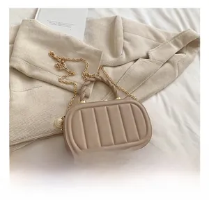 Close-up of quilted beige crossbody bag with woven gold handle and pearl pendant