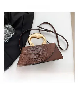Detail of dark brown handbag with crocodile texture and sculptural golden metal handle