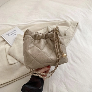 Quilted beige bucket bag with gold chain strap and drawstring closure in casual setting