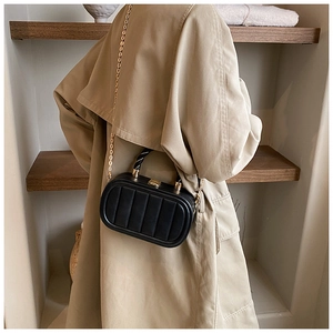 Fashionable black quilted box bag with gold chain strap shown on khaki trench coat