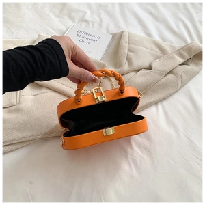 Detail view of orange crossbody bag with twist handle, gold clasp, and interior space