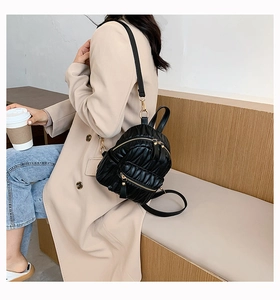 Detail of a black quilted mini backpack with gold hardware worn in a street style setting