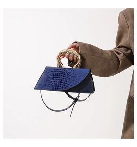 Detail of navy blue crocodile pattern leather handbag with curved gold metal handle