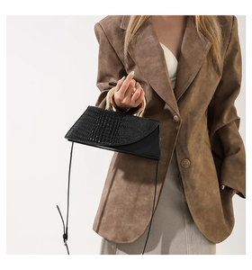 Detail of black crocodile texture bag with gold metal handle on brown blazer