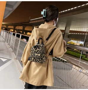 Detailed back view of a mini leopard print backpack with gold zippers in outdoor street scene