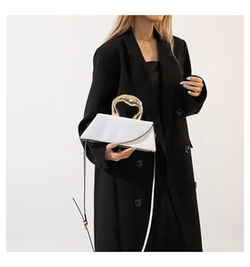 White croc-effect flap bag with unique gold handle held by model in black blazer
