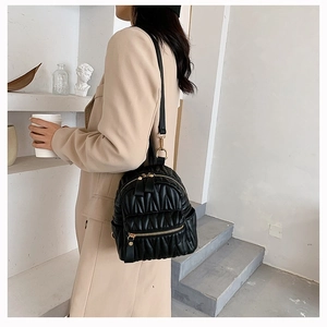 Quilted black mini backpack with wavy pleats and gold hardware in a minimalist setting