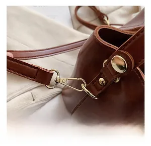 Détail du crochet en métal doré et de la bandoulière en cuir marron d'un sac seau