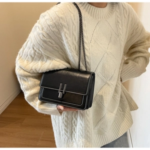 Detail of black crossbody chain bag with metal lock and white contrast stitching