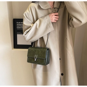 Detail of dark green retro PU leather crossbody bag with silver chain on beige trench coat