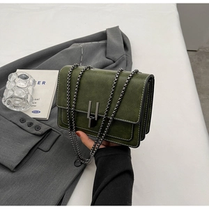 Detail of dark green leather shoulder bag with white contrast stitching and metal chain