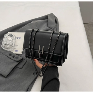 Detail of black crossbody bag with white contrast stitching and U-shaped buckle closure