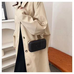 Detail view of a black evening clutch with gold metal frame on a beige coat outfit