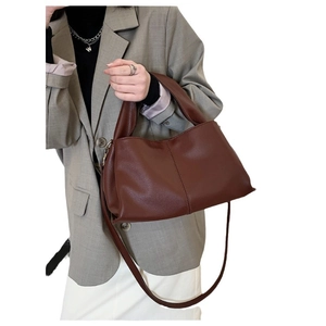 Chic brown leather crossbody bag with top handle worn by model in gray blazer