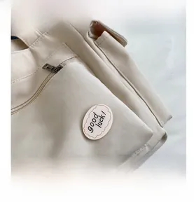 Detail of off-white canvas bag featuring a front zipper pocket and 'good luck!' patch