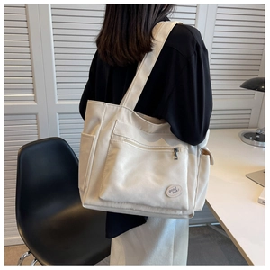 Detail of off-white canvas tote bag featuring multi-pocket design and good luck patch