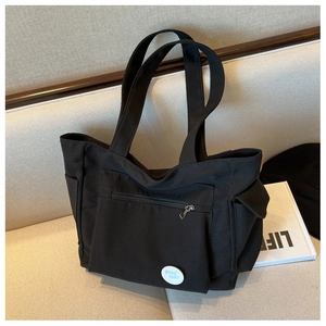 Detail of black canvas tote bag featuring a front zipper pocket and round lucky badge