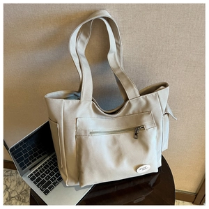 Detail of beige canvas tote bag with zip pocket and embroidered good luck patch