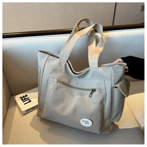Detail of canvas tote bag showing side flap pocket and good luck patch on beige fabric