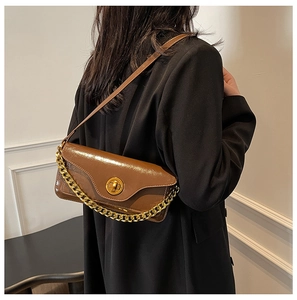 Detail of vintage brown shoulder bag with gold chain and wax leather texture on black blazer
