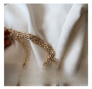 Detail of multi-layer golden metal chain strap with high-gloss finish on white textured fabric