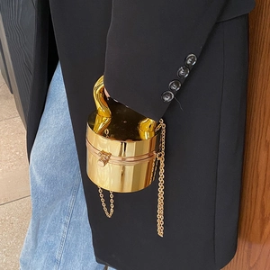 Close-up of golden cylindrical evening bag with metal handle and detachable chain strap
