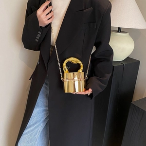 Close-up of golden cylinder handbag featuring mirrored finish and twisted metal handle