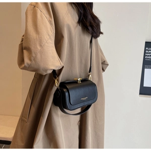 Petit sac à bandoulière en cuir noir avec boucle dorée porté sur un trench-coat classique