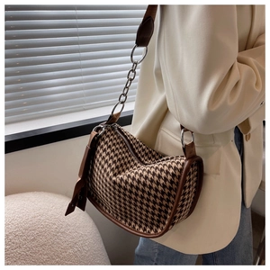 Detail of houndstooth crossbody bag with brown leather trim and metal chain strap
